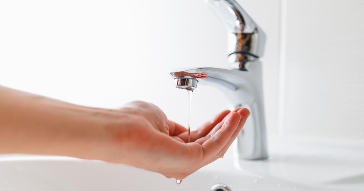 Hand under a running faucet, catching water in a white sink