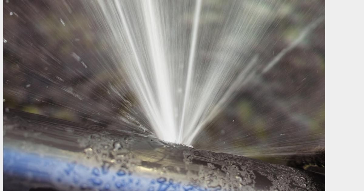 Water spraying from a pipe onto a dirty surface, creating a bright fan of mist