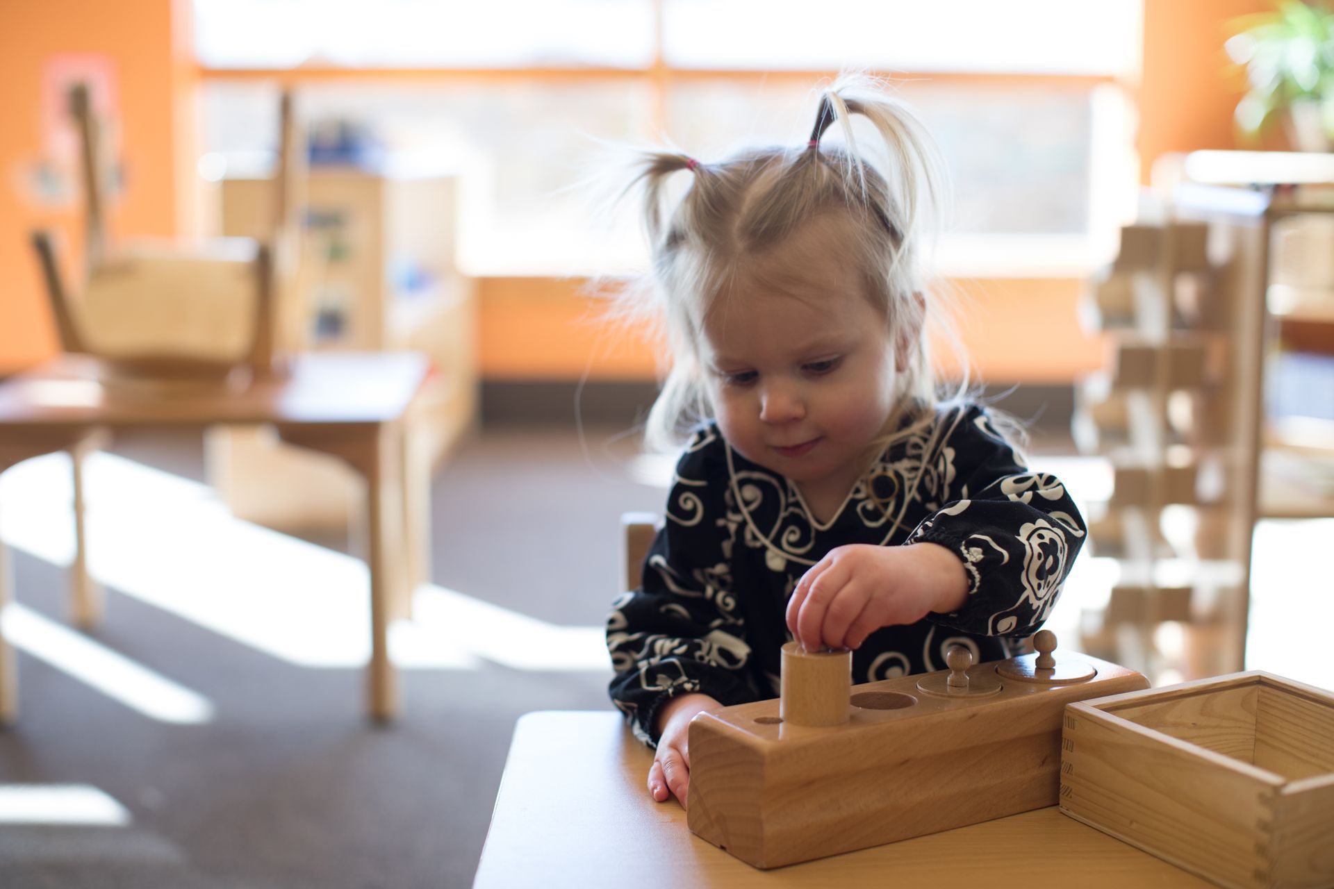 Toddler playing with wooden blocks at a table in a bright classroom