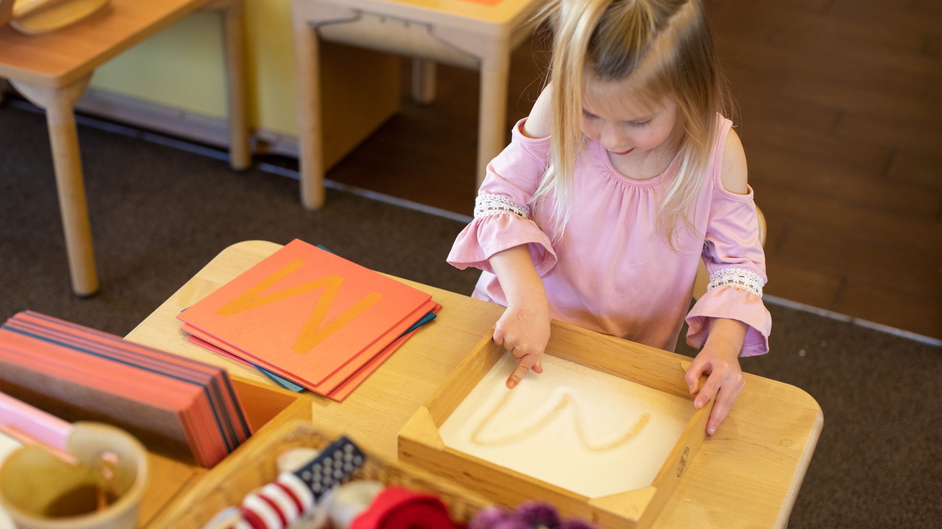 Child in a pink dress using a sand tray at a classroom table