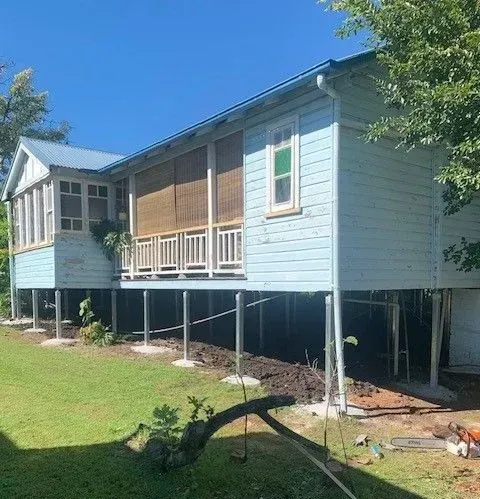 Elevated light-blue house on stilts with a porch and grassy yard