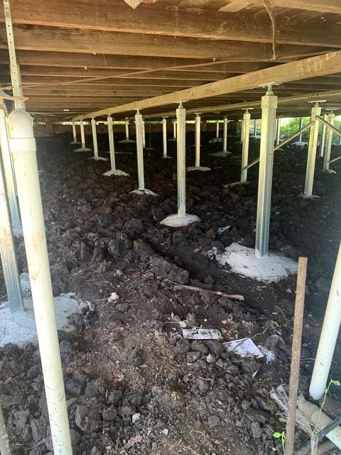 Crawl space under a wooden house with many support posts and exposed dirt floor