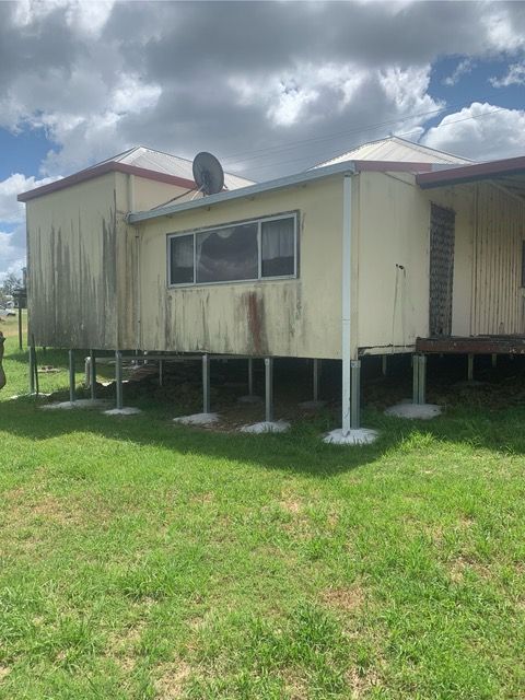 Small elevated house on stilts in a grassy yard under a cloudy sky, with a satellite dish on the roof.