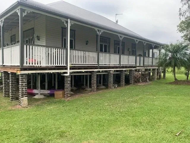 Raised gray house with white porch railings on brick piers, beside a grassy yard