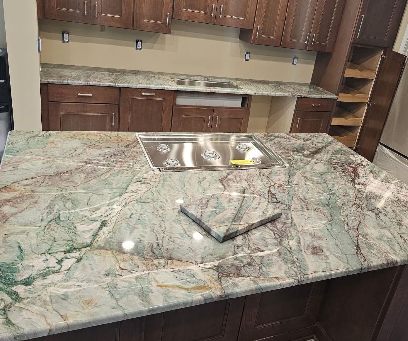 Kitchen with green and white granite island countertop and brown cabinets. Stainless steel stovetop.