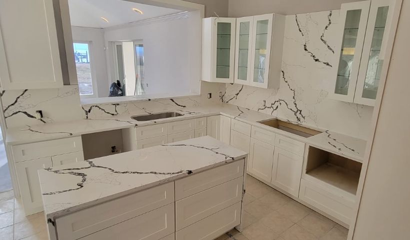 White kitchen with quartz countertops, cabinets, and island; a cooktop and sink are present.
