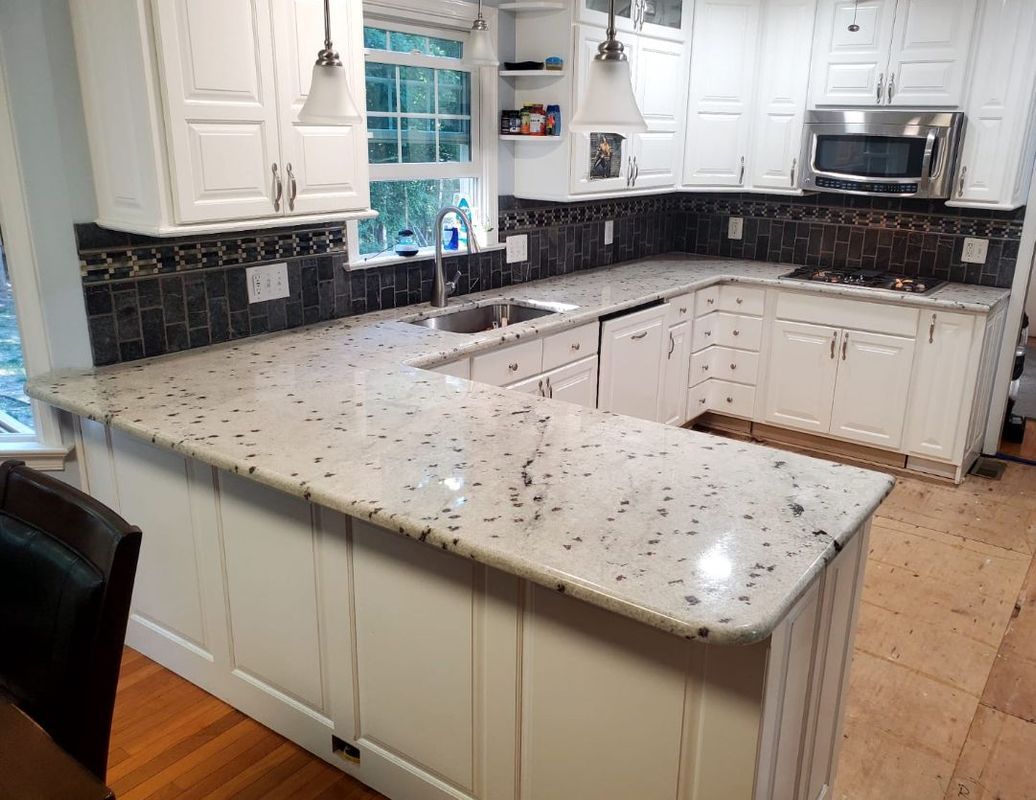 White kitchen with granite countertops, black tile backsplash, and stainless steel appliances.