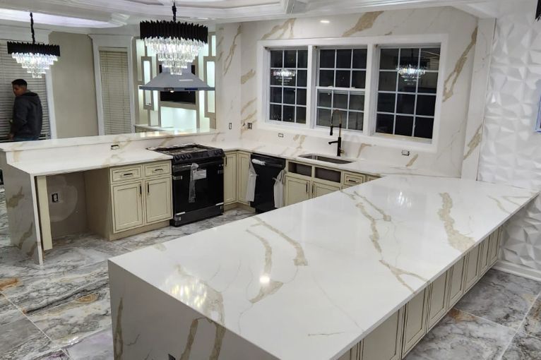 Luxurious kitchen with white and gold countertops, black appliances, cabinets, and ornate chandeliers.