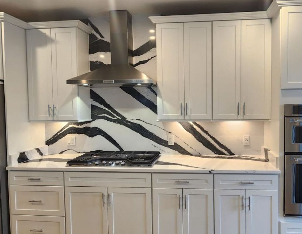 White kitchen with bold black and white backsplash and stainless steel vent hood.