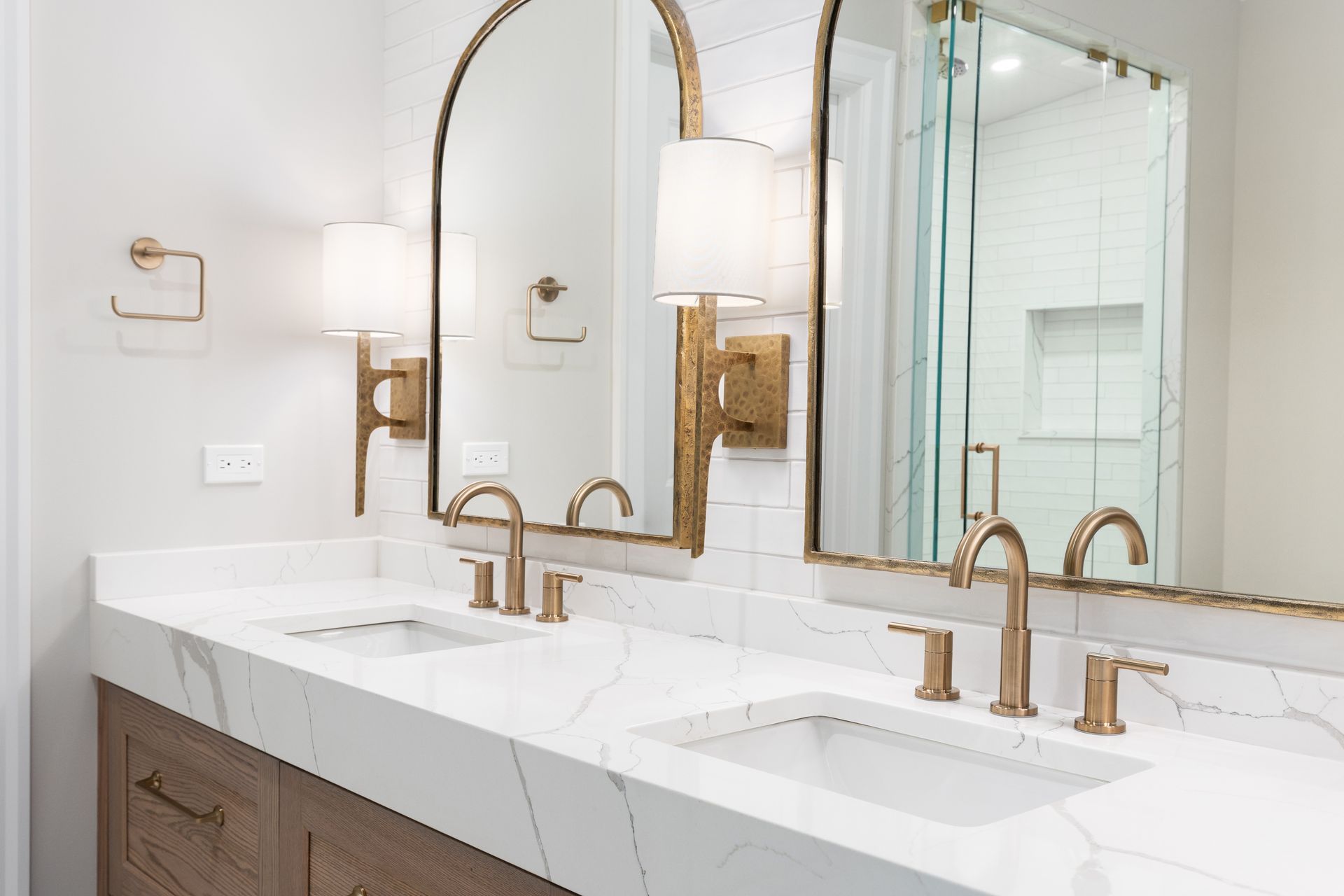 Bathroom vanity with marble countertop, two sinks, arched mirrors, and gold fixtures. Bathroom vanity with marble countertop, two sinks, arched mirrors, and gold fixtures.