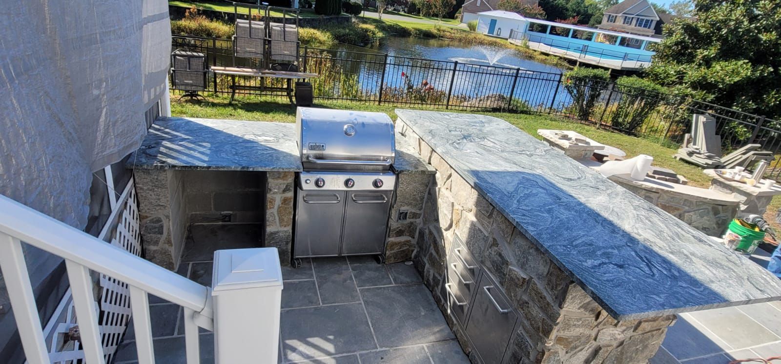 Outdoor kitchen with stainless steel grill, stone countertop, and pond view.