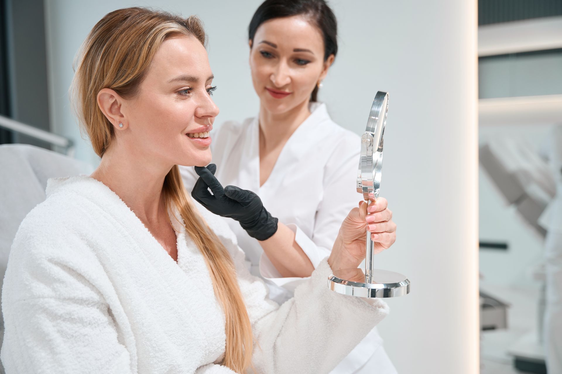 A woman is looking at her face in a mirror in a beauty salon.