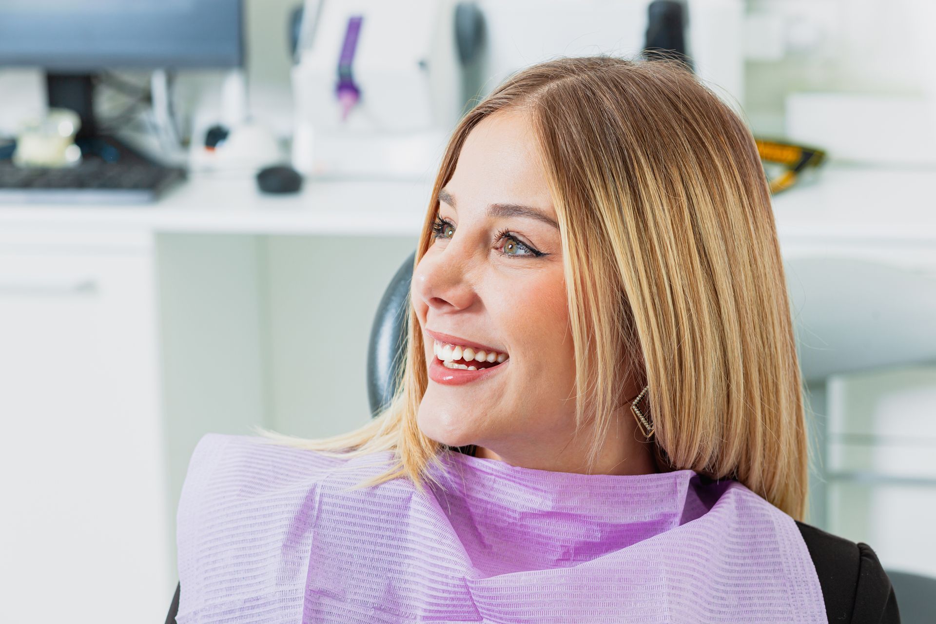 A woman is smiling while sitting in a dental chair.