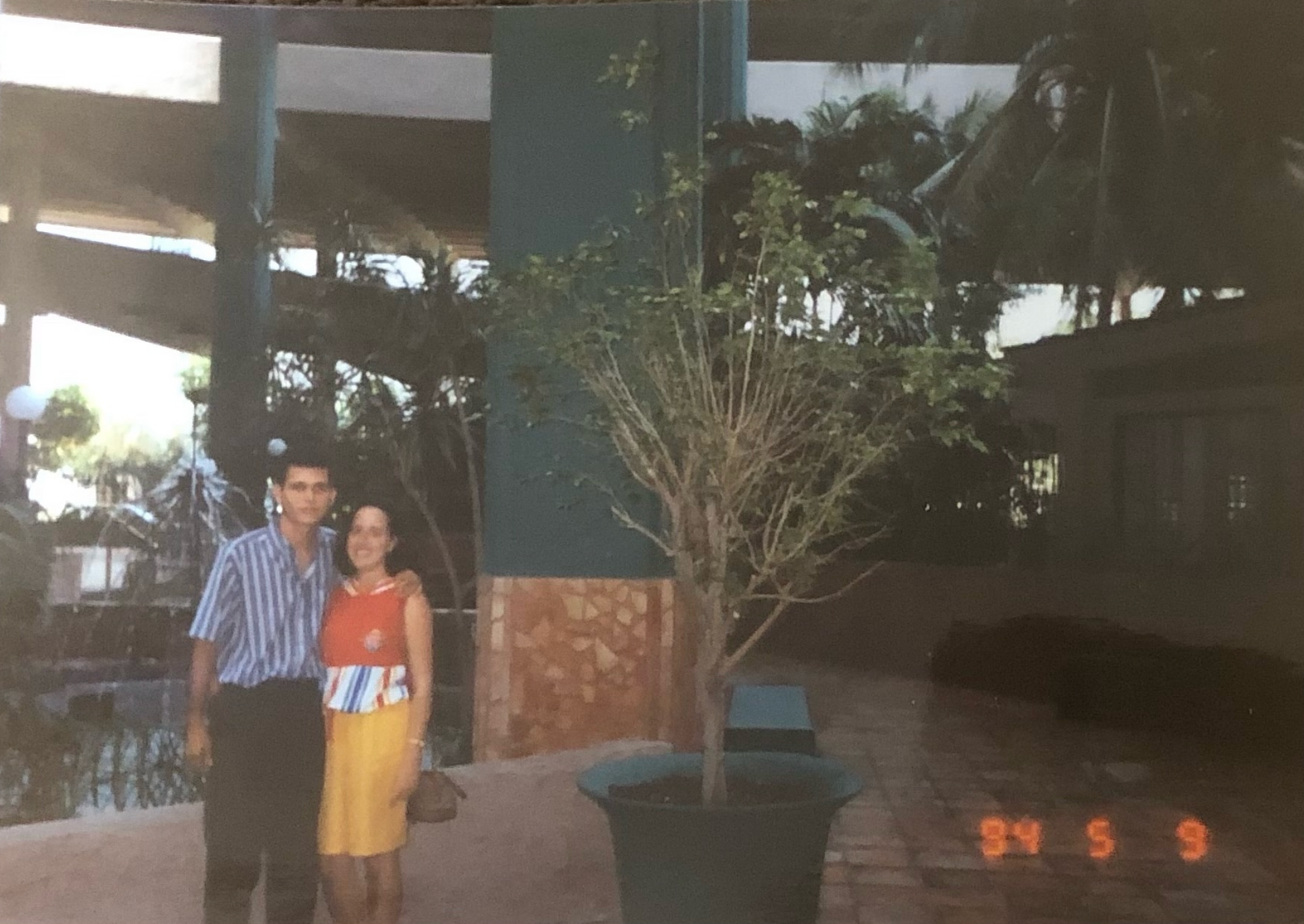 A man and a woman pose for a photo in front of a tree in a pot