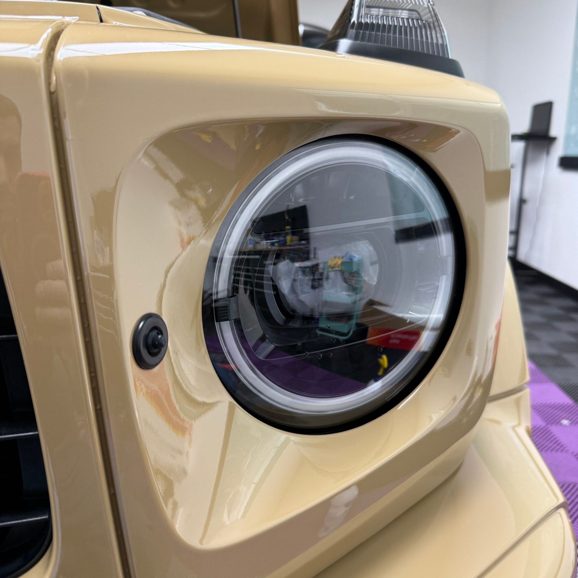 Close-up of a tan Mercedes-Benz G-Wagon headlight, showing the round headlight with a black bezel.