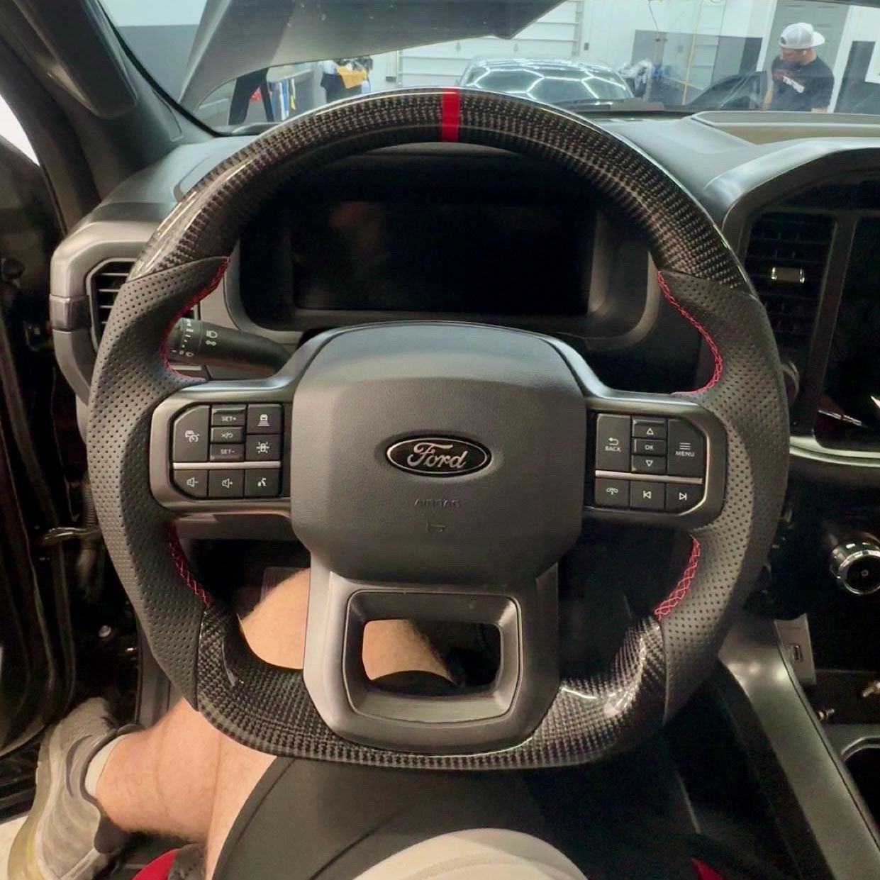 Close-up of a carbon fiber Ford steering wheel with red stitching and a red stripe at the top.