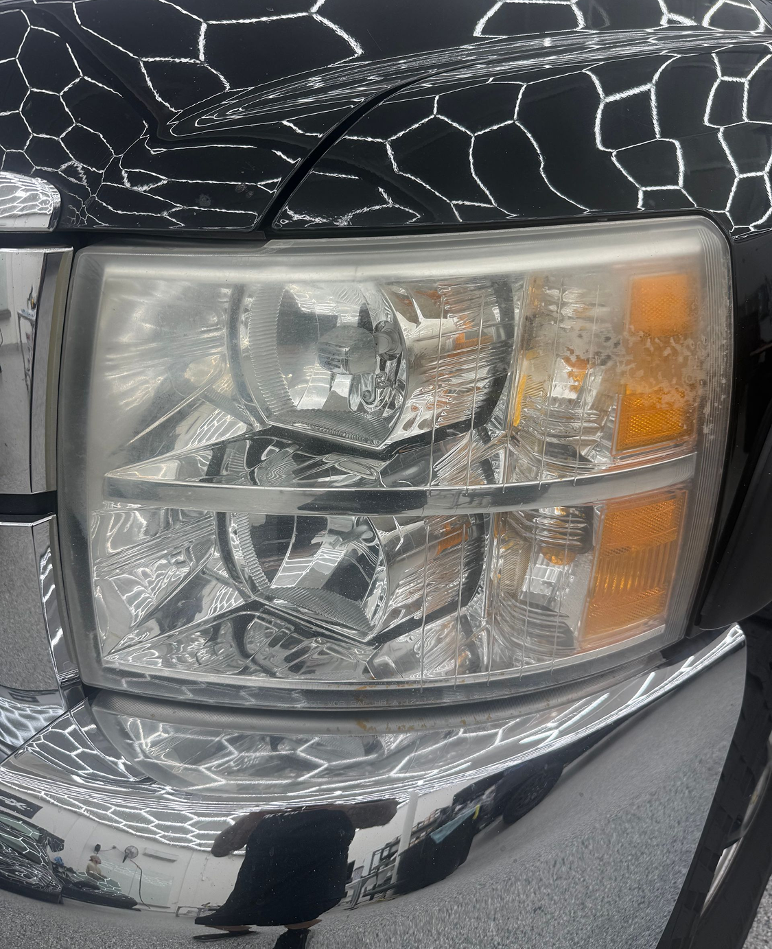 Close-up of a cracked truck headlight and chrome bumper on a black vehicle