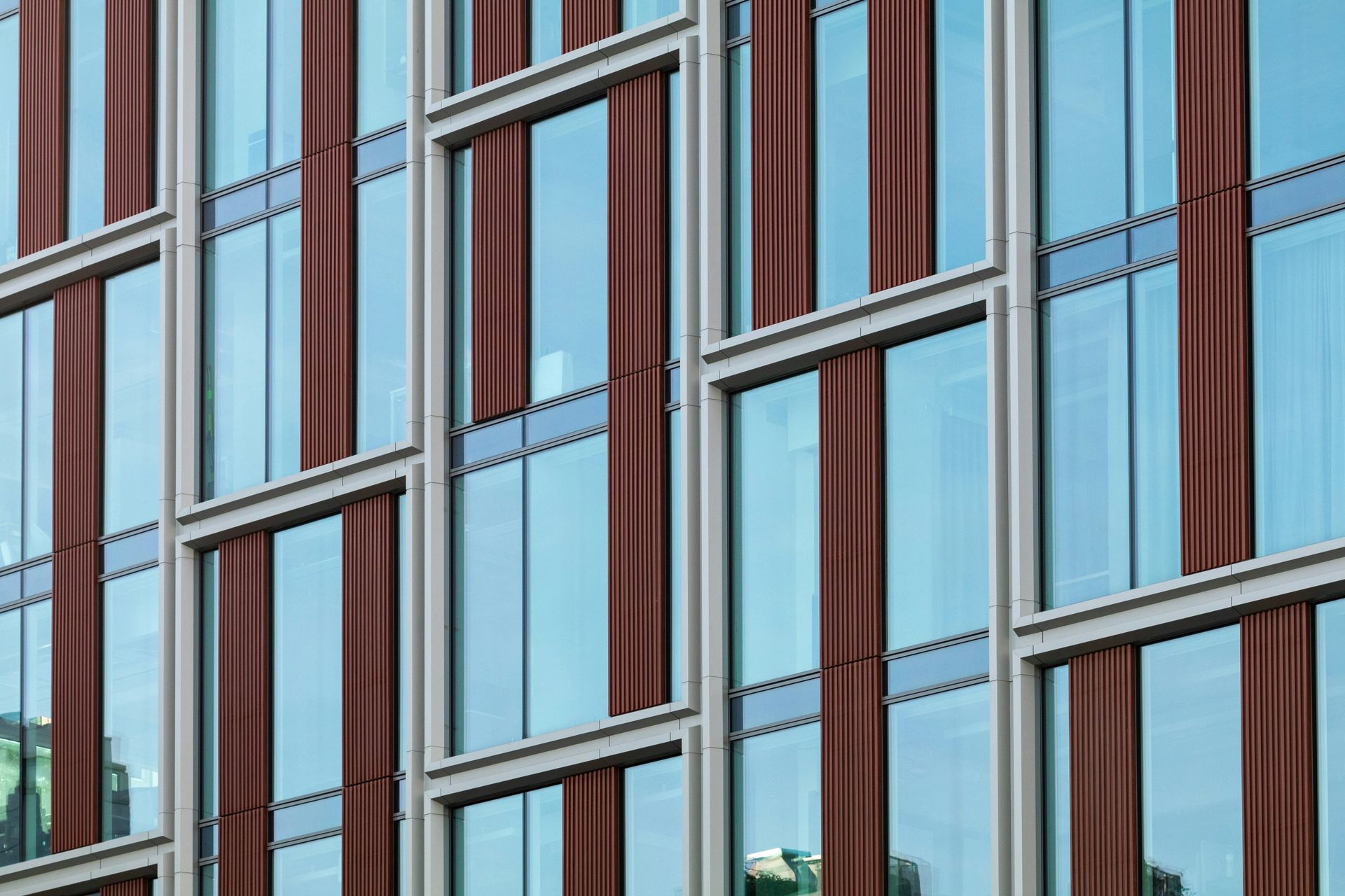 Modern building facade with alternating glass windows and reddish-brown vertical panels.