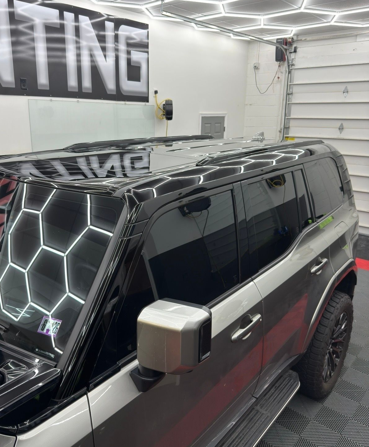 Black SUV parked inside a garage, with bright white hexagonal lights on the ceiling.