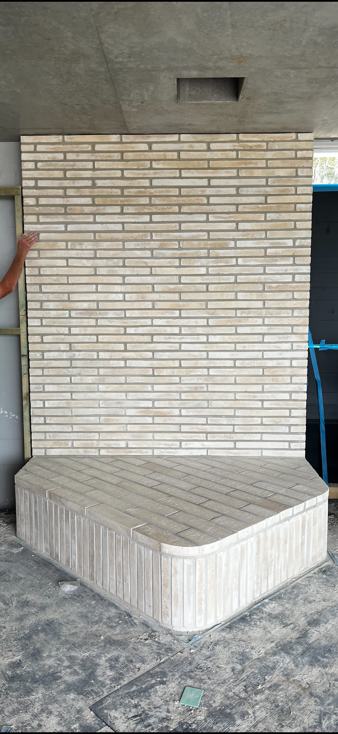 A person is standing in front of a brick wall.
