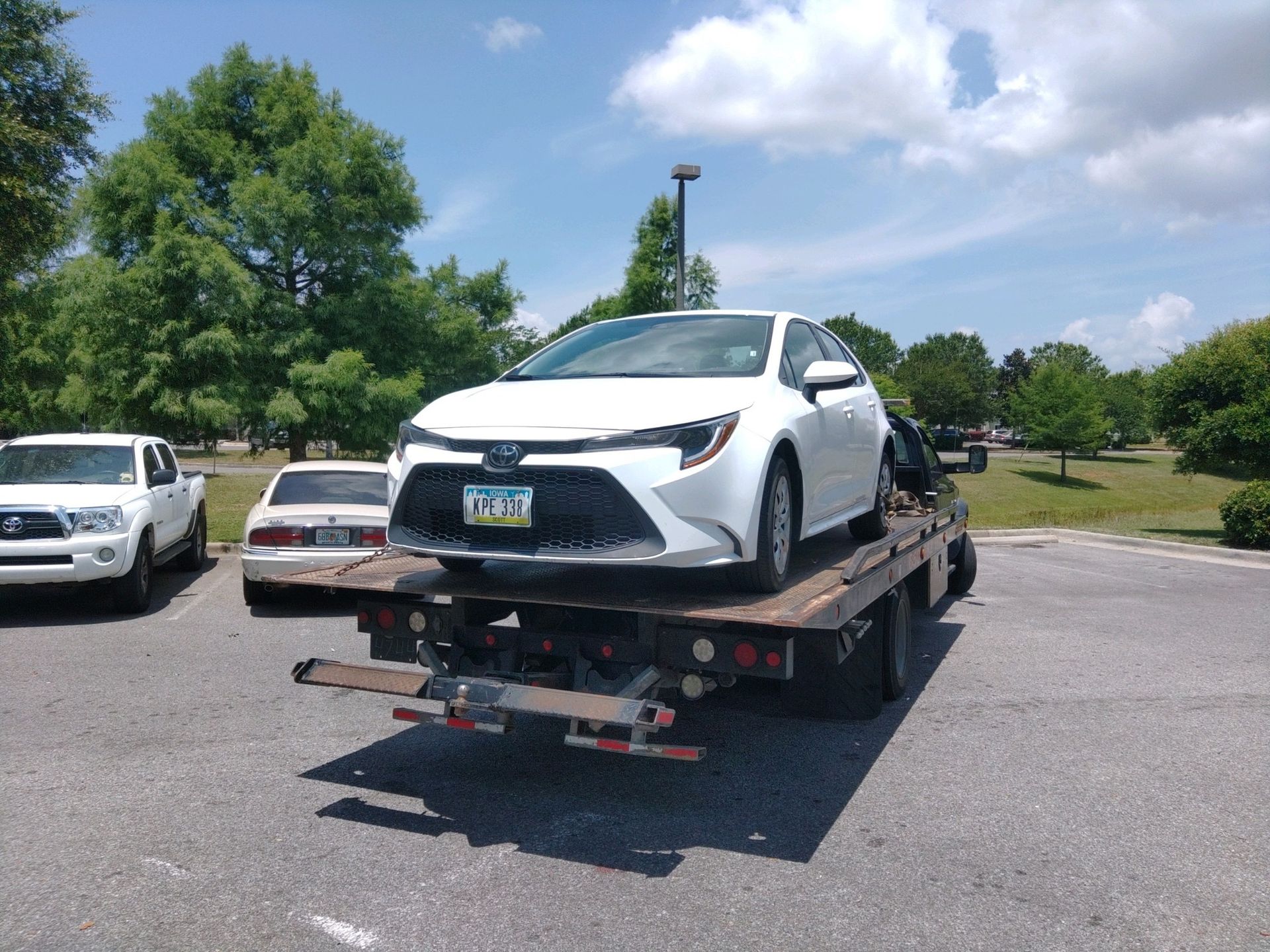 White compact SUV on a flatbed tow truck in a sunny parking lot.