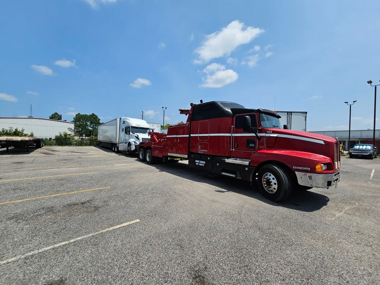 Red tow truck and trailer parked in an open lot under a blue sky