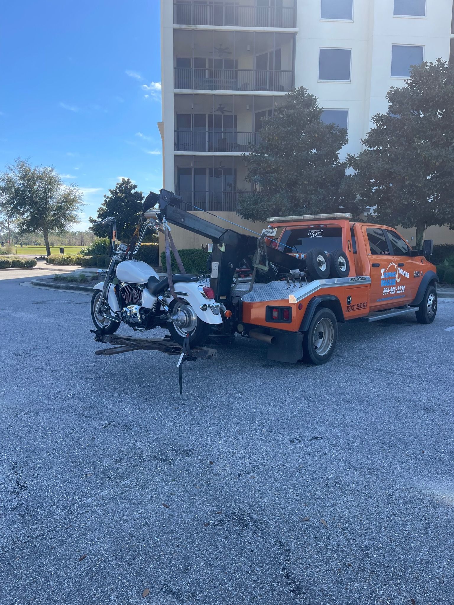 Orange tow truck lifting a motorcycle in a gravel lot beside an apartment building.