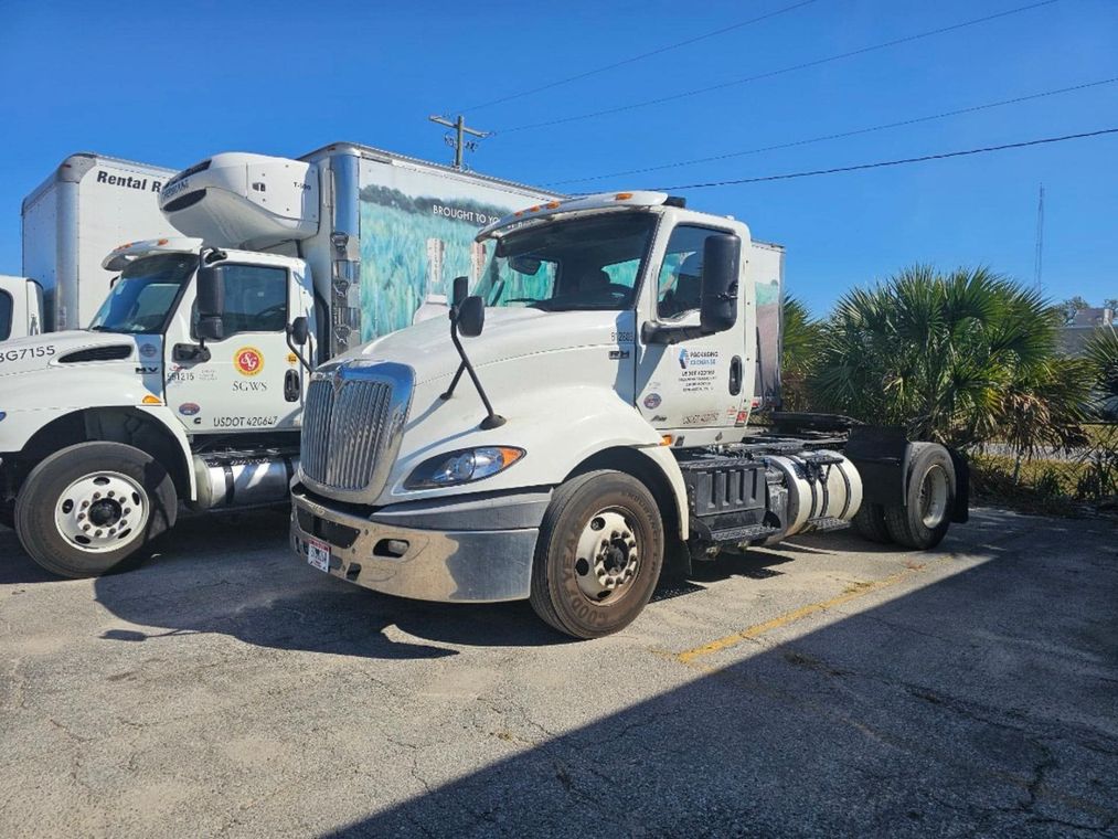 Two white semi-trucks parked side by side in a sunny lot under a clear blue sky