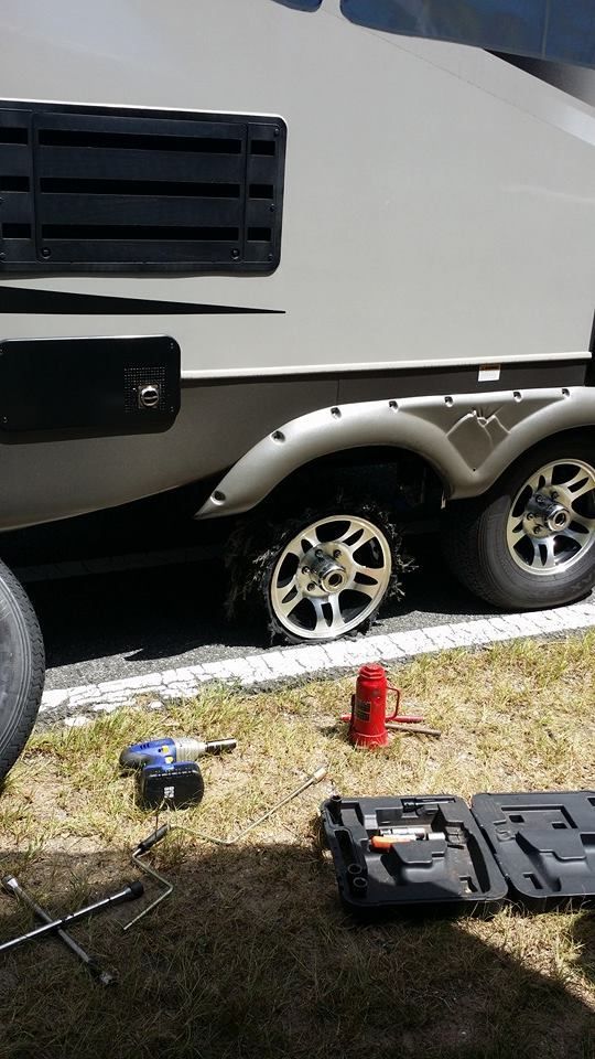 White RV trailer with silver wheels parked on grass, with tools and a red jack in front