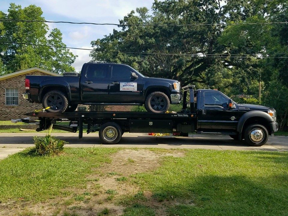 Black pickup on a tow truck in a grassy yard, with trees and houses in the background.