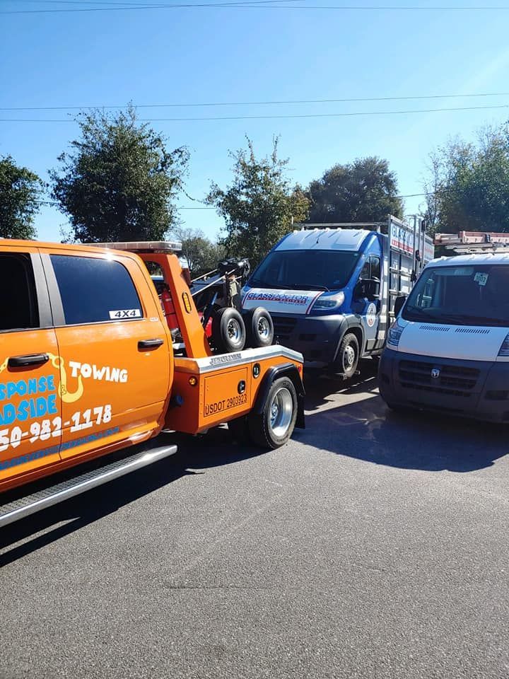 Tow truck hauling a blue van and a gray van on a sunny road