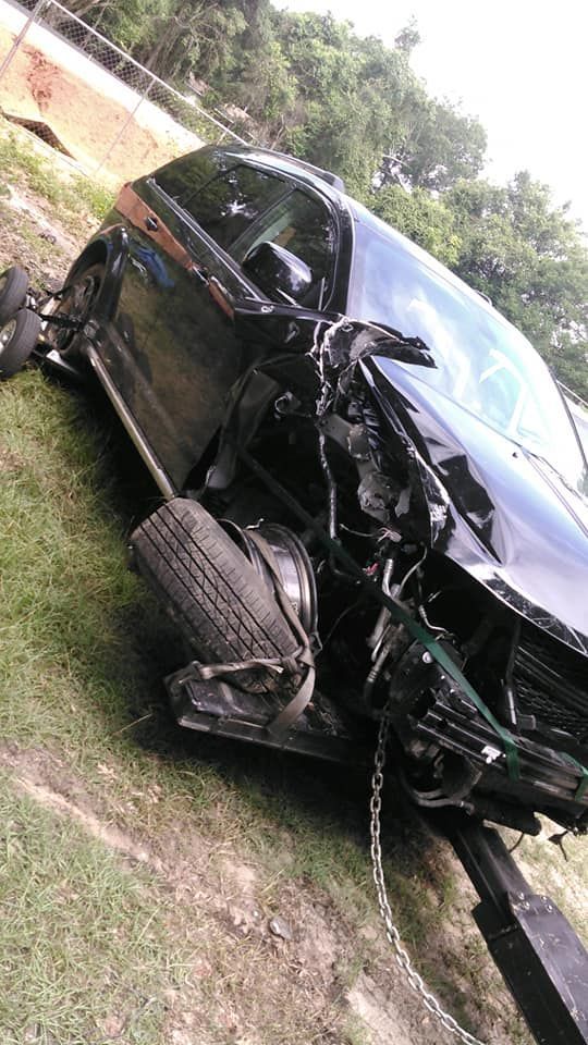Black SUV with severe front-end crash damage on a grassy roadside.