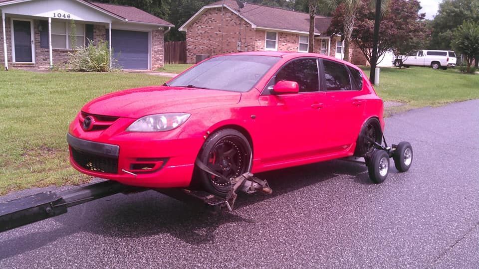 Red car on a tow dolly after a rear wheel break, parked on a residential street.