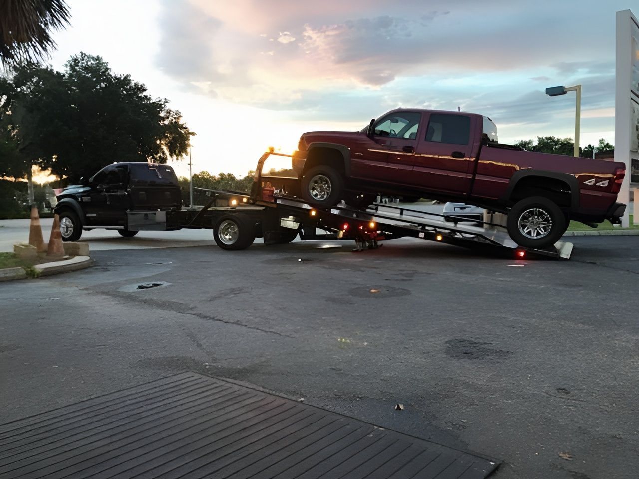 Two pickup trucks on a flatbed tow trailer at sunset in a parking lot