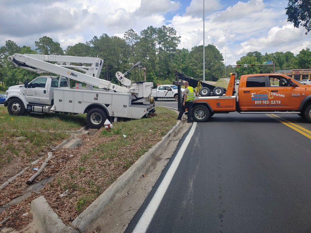 White tow truck and orange utility truck on roadside after crash, with workers nearby.