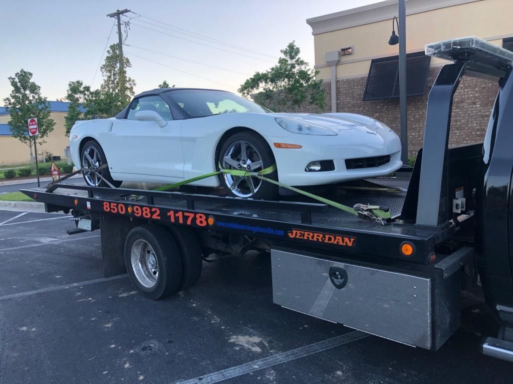 White sports car strapped on a flatbed tow truck in a parking lot outdoors.