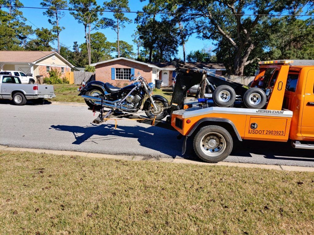 Orange tow truck hauling a wrecked motorcycle on a suburban street