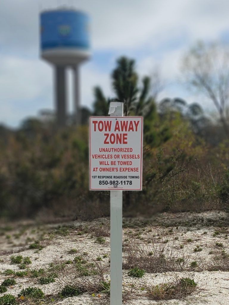 Tow away zone sign in sandy brush with a blue water tower blurred in the background