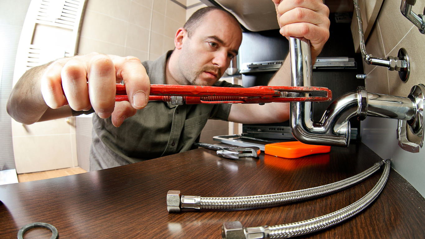 A man is fixing a pipe with a wrench.