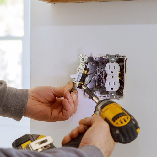 A man is installing an electrical outlet with a drill
