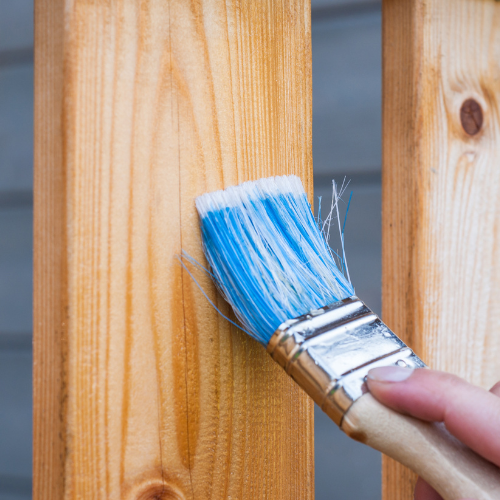 A person is painting a wooden post with a blue brush.