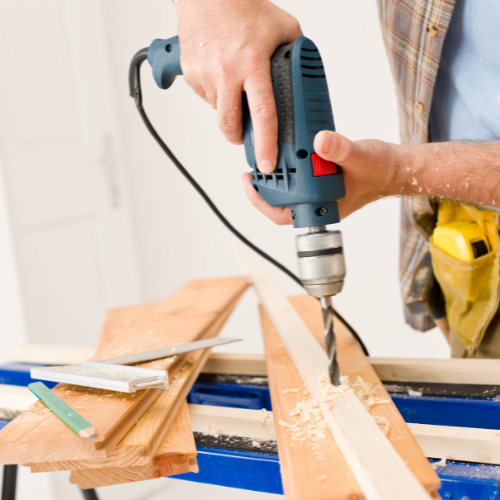 A man is using a drill to drill a hole in a piece of wood
