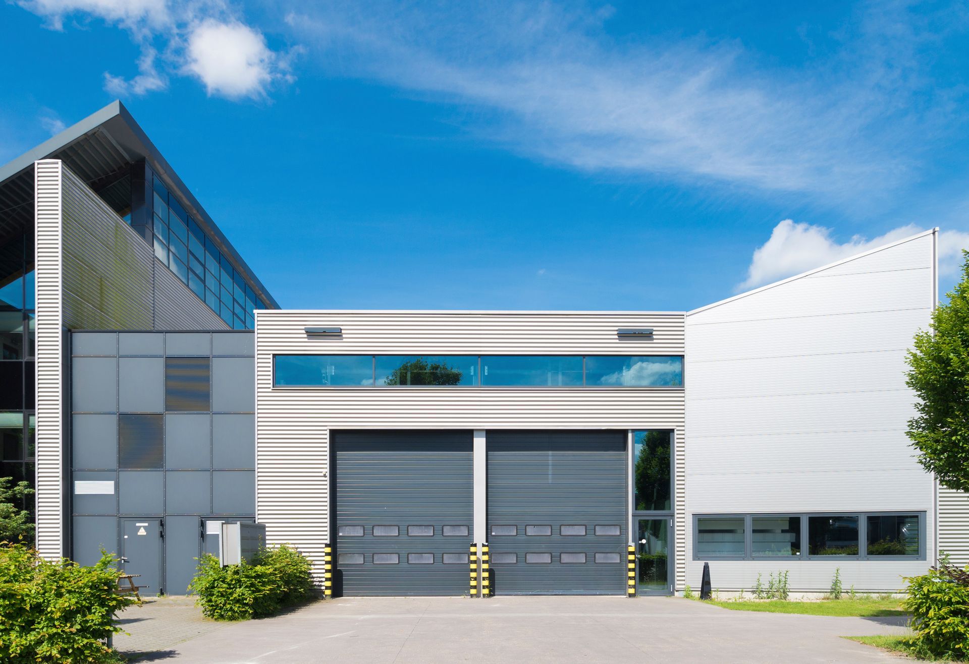 Modern industrial warehouse or commercial building with two loading bay doors under a blue sky. Modern industrial warehouse or commercial building with two loading bay doors under a blue sky.