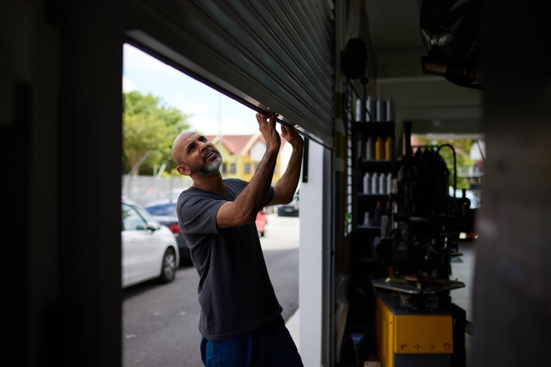 mechanic opening shutter door to car workshop