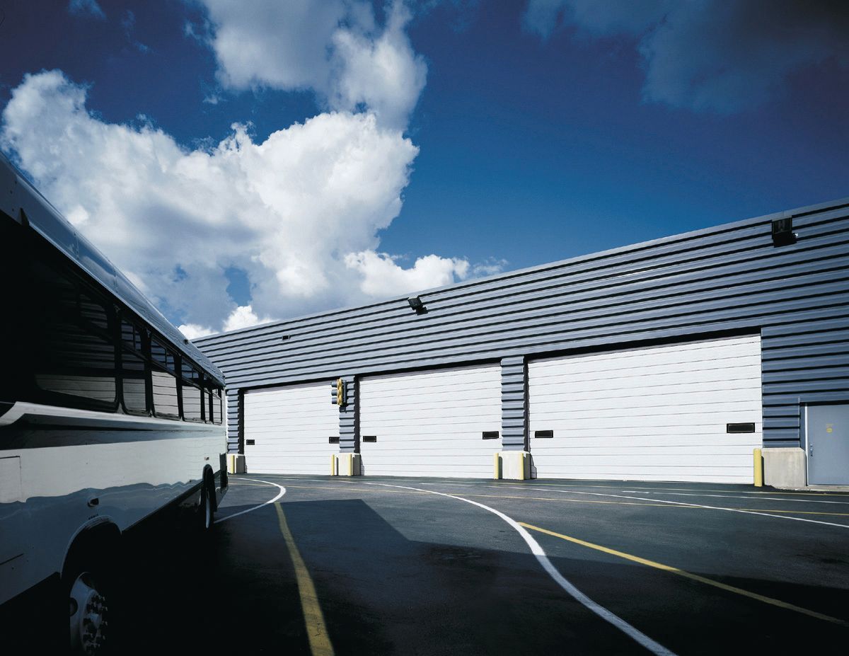 A bus is parked in front of a building with white garage doors.