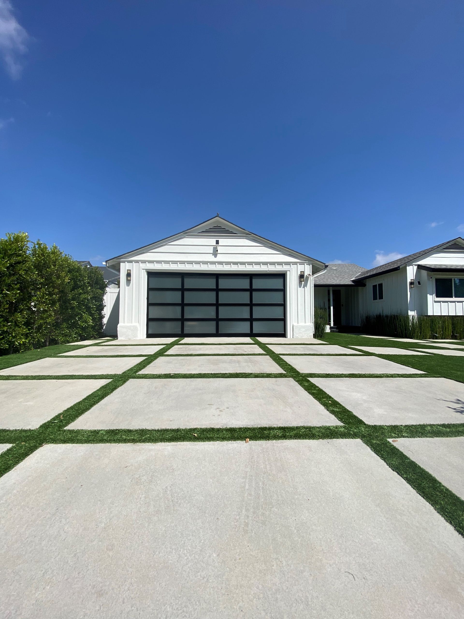 A white house with a garage door and purple flowers in front of it.