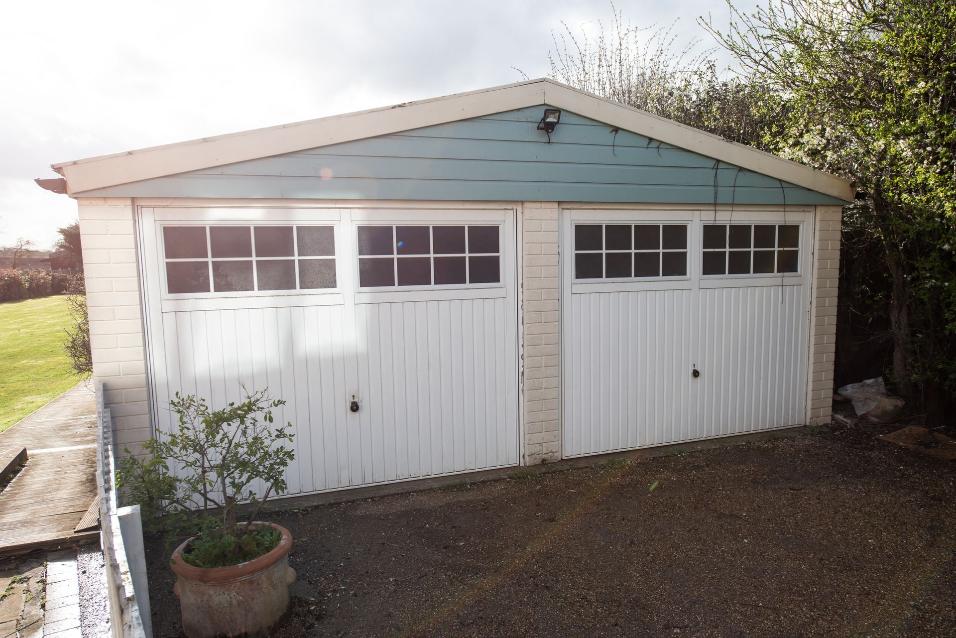 Detached garage with two white doors and windows, set against a light blue gable roof.