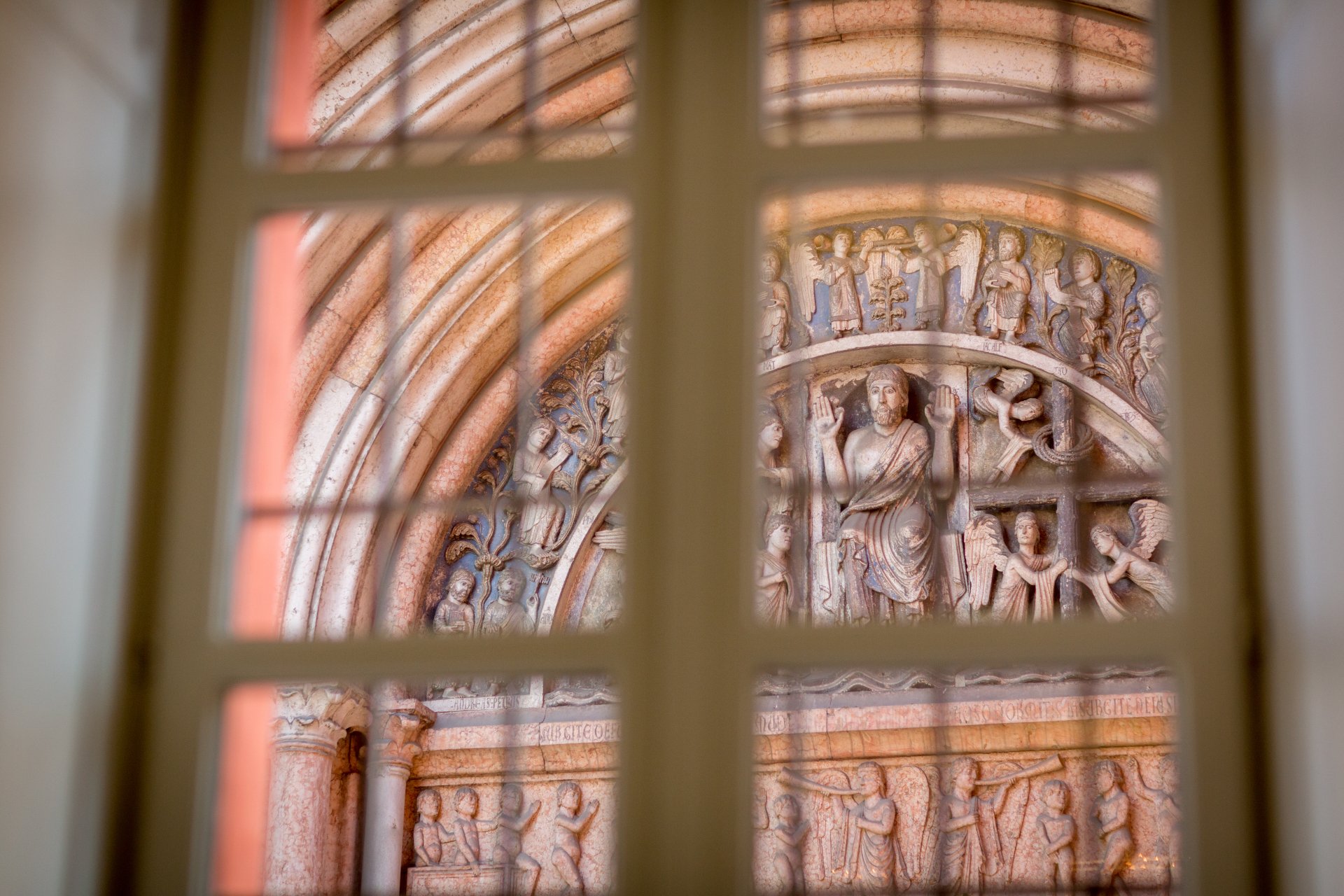 View of an ornate archway through a window; reddish-brown stonework, figures, and arches.
