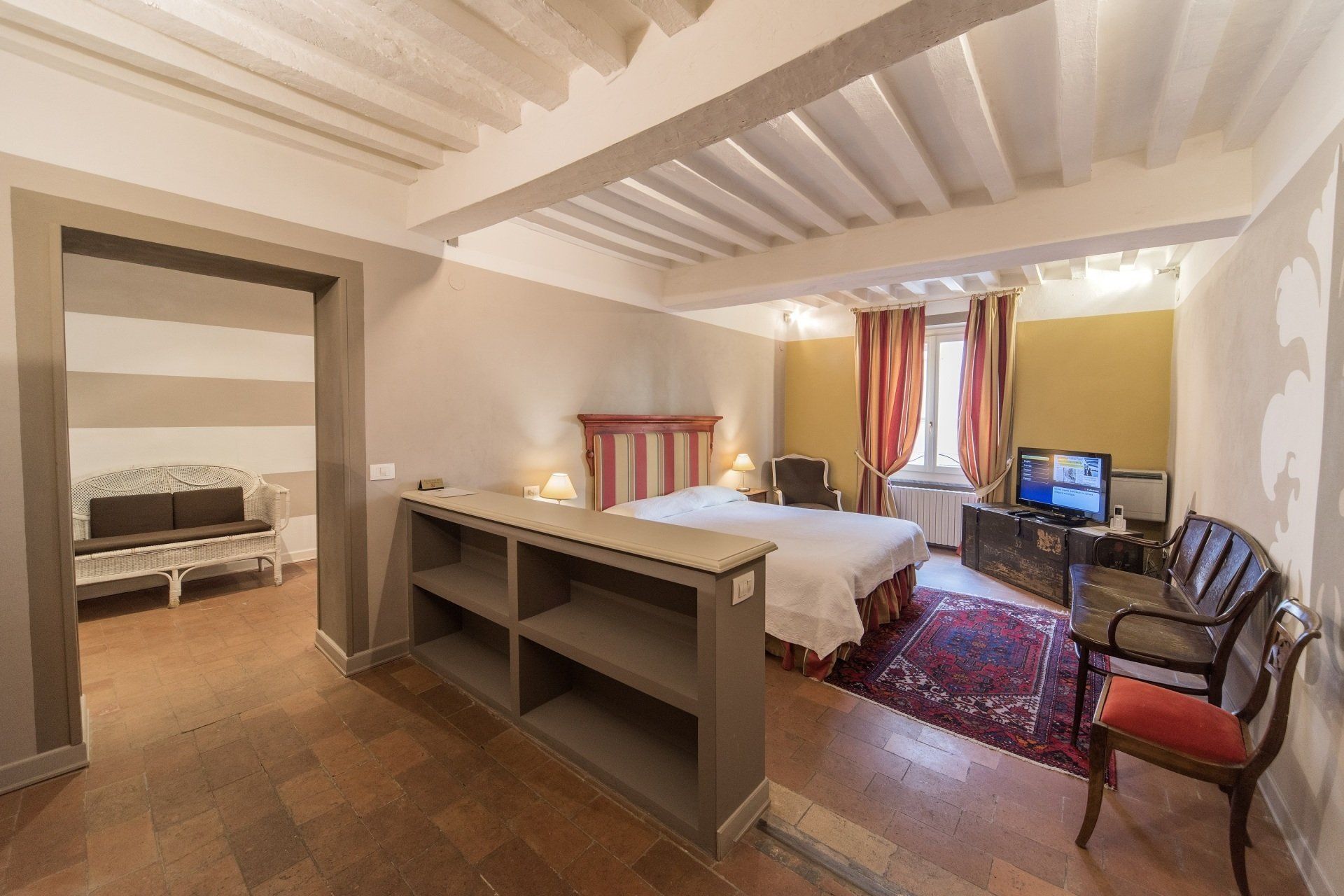 Camera da letto con letto, zona soggiorno, tappeto rosso, TV e porta aperta su un soggiorno con divano.