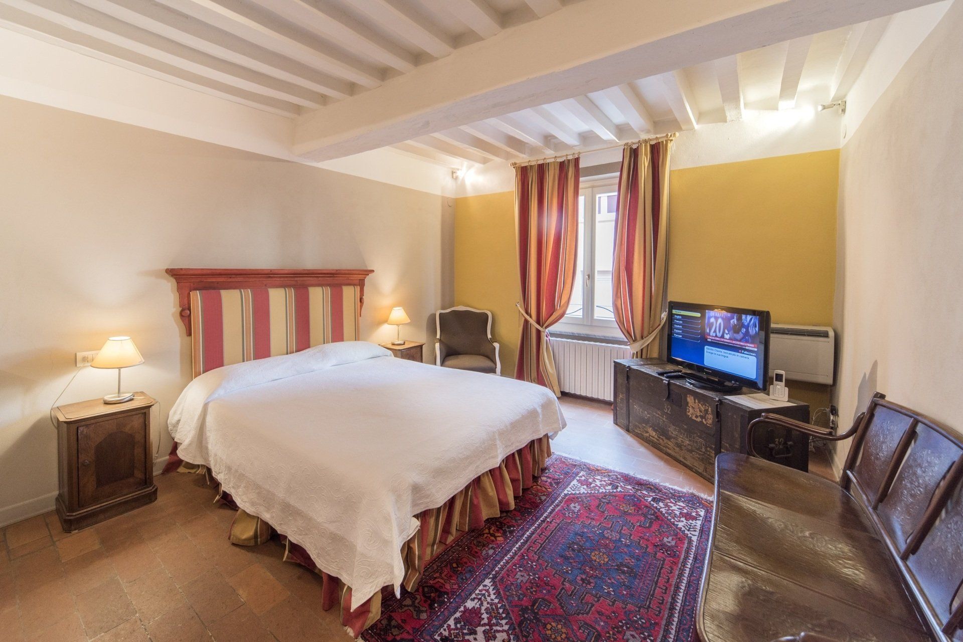 Camera da letto con letto, mobili antichi, TV e finestra con tende.